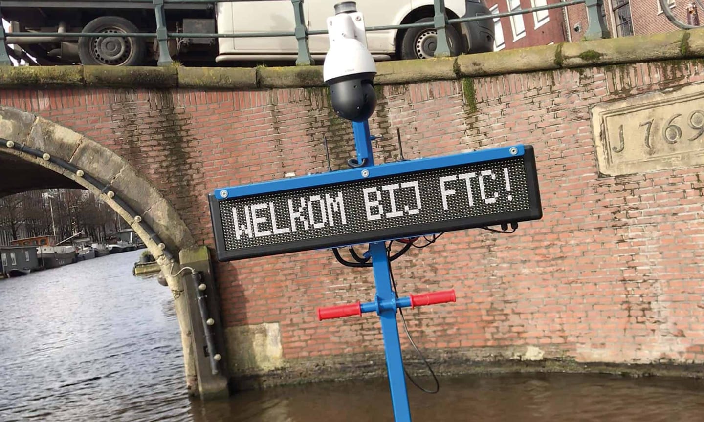 Contact RRB Security: koepelcamera op een paal bij een gracht met een bord WELKOM BIJ FTC!