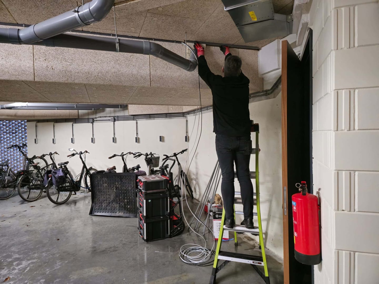 Contact RRB Security: monteur op een trapladder legt kabels aan het plafond van een fietsenstalling